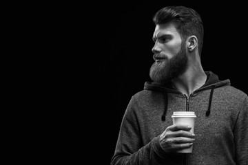 Black and white dramatic light studio shot of young caucasian bearded stylish man with cup of...