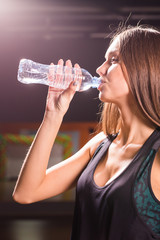 Fitness young woman drinking water from bottle. Muscular young female at gym taking a break from workout.