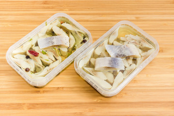 Slices of pickled herring in two containers with different marinades