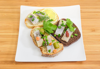 Three different open sandwiches with pickled herring fillet on dish