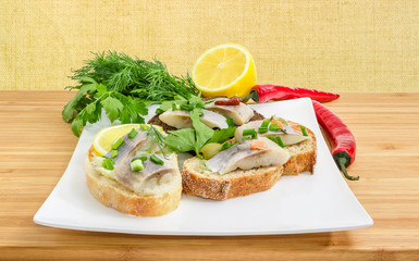 Various open sandwiches with pickled herring fillet on square dish