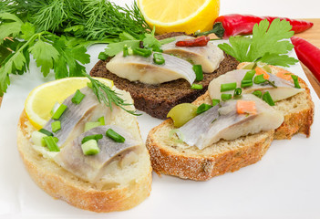 Various open sandwiches with pickled herring fillet on dish closeup