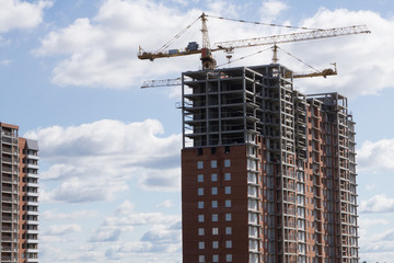 Fototapeta premium Photos of high-rise construction cranes and unfinished house against the blue sky with clouds. Taken from the bottom up .