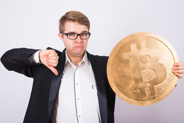 Unhappy man holding a golden bitcoin and showing thumbs down. Cryptocurrency crash concept