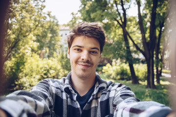 handsome young man looking at the camera and taking a selfie photo outdoors. 