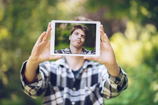 detail shot of an attractive and handsome young man taking a selfie with a tablet, making a silly spontaneous face.