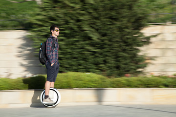  A stylish guy moves along the sidewalk on a mono-wheel.