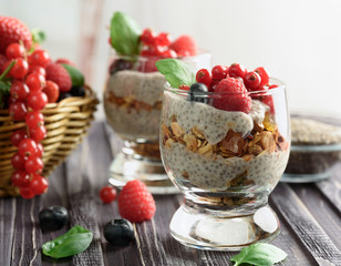 Two glasses of chia pudding with fresh strawberries, raspberries and blueberries. Basket with...