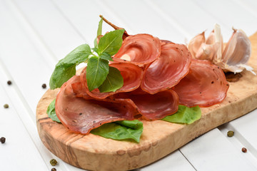 Salami smoked sausage slices basil leaves and peppercorns on white background