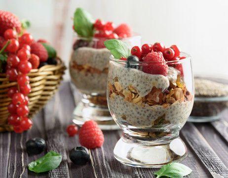Two glasses of chia pudding with fresh strawberries, raspberries and blueberries. Basket with berries.