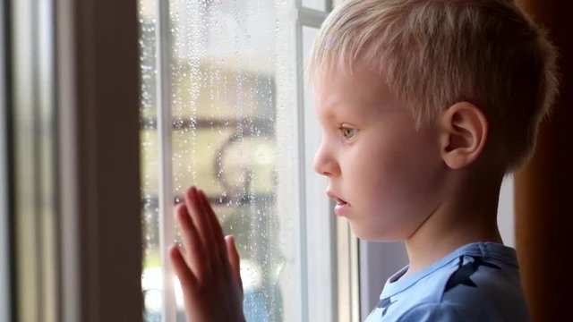 Little boy looking at the window covered with drops of rain