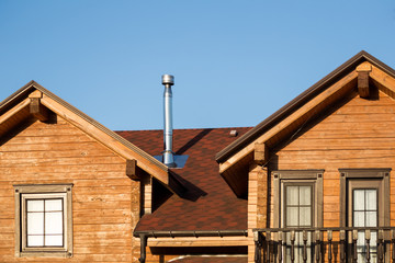 Part of modern wooden country house with blue sky on background. Roof of eco residential building near forest. Building and architecture of rustic chalet