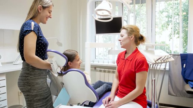 4k footage of female dentist talking to young mother and teenager girl sitting in dental chair