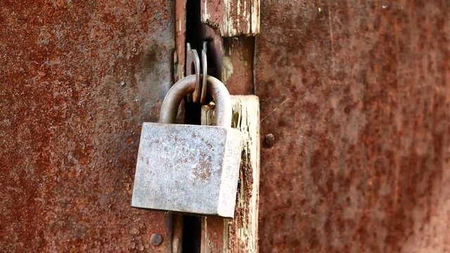 Closeup of old lock on red metal garage door. Rusty lock on an old wooden gate. Old padlock on closed doors