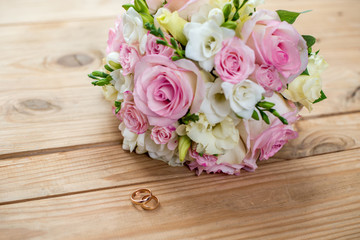 Two gold wedding rings and beautiful wedding are on the brown wood table