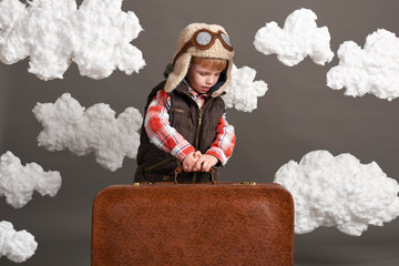 boy dressed as an airplane pilot stand between the clouds with old suitcase and playing with handmade plane