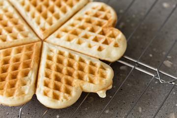 Freshly backed waffles in shape of heart, resting on metal rack close up