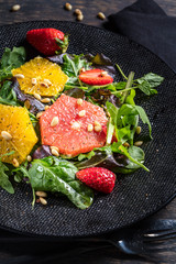 Grapefruit and orange mix salad with pine nuts on black plate and dark background. Vertical composition