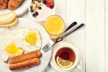 Breakfast of sunny side up eggs, sausages, orange juice, tea, and fruits