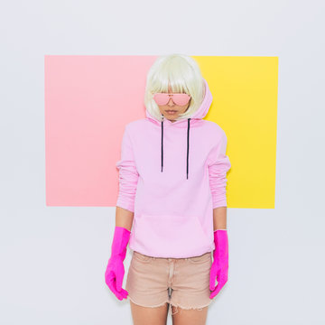 Doll Blonde Girl Model in the hood with Fashion accessory sunglasses, gloves,  hoodie and shorts.  Minimal unicorn style. Pink and yellow neon colors. 90s or 80s trend