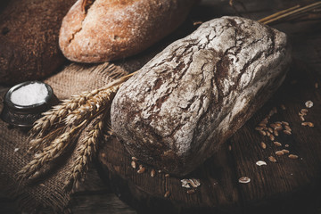 Rustic bread and wheat on an old vintage planked wood table. Dark moody background with free text space.