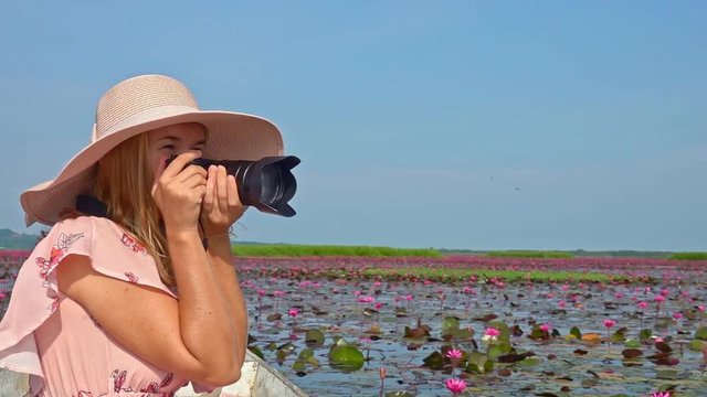 Female Tourist in Hat Riding Boat and Taking Photos of Red Lotus Flowers. Young Woman Visiting Thale Noi Waterfowl Reserve Lake, Thailand