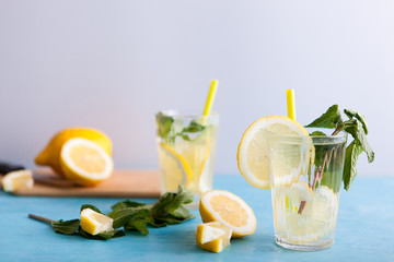 Two glasses with delicious homemade lemonade on gray background sitting on blue desk