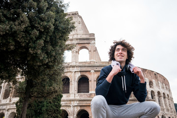 Fototapeta na wymiar Handsome young sportsman relaxing after training with a towel around his neck in front of Colosseum in Rome