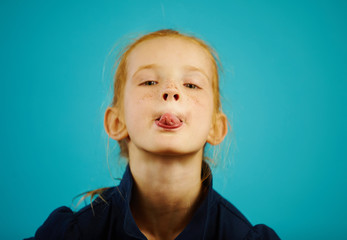 Close-up portrait of naughty redhead girl on blue isolated background shows you the tongue and...