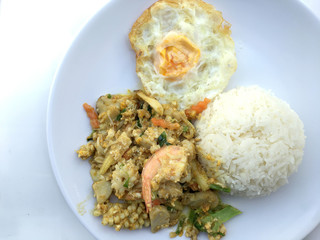 Stir-fried seafood, prawn and squid with yellow curry powder with rice and fried egg in white plate on white background. Thai style food.