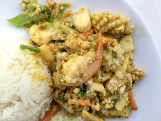 Stir-fried seafood, prawn and squid with yellow curry powder with rice and fried egg in white plate on white background. Thai style food.