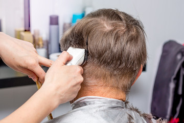 Fototapeta premium Hairdresser makes stylish hairstyle for an elderly man_