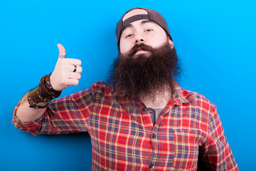 Man with long beard showing thumbs up to the camera on blue background