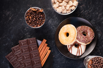 Top view of chocolate tablets, donuts, brown sugar with peanuts in chocolate and coffee beans on dark vintage wooden background