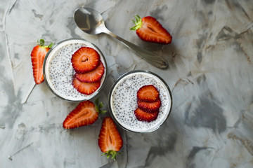 Two servings of dessert made of chia seeds, milk and strawberries on a gray table. Healthy Breakfast Concept. Top view