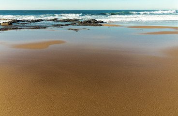 Fototapeta na wymiar Golden Beach Sand Rocks and Reflections Against Blue Skyline