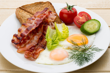 Fried eggs with bacon on the wooden table.