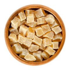 Candied ginger root cubes in wooden bowl. Crystallized roots of Zingiber officinale. Orange colored rhizomes, preserved with sugar. Snack. Macro food photo close up from above on white background.