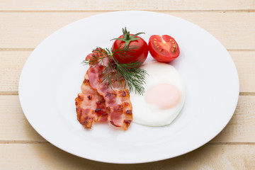 Fried eggs with bacon on the wooden table.