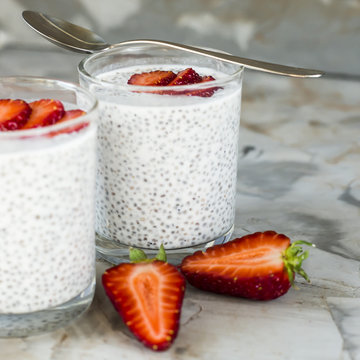Two servings of dessert made of chia seeds, milk and strawberries on a gray table. Healthy Breakfast Concept