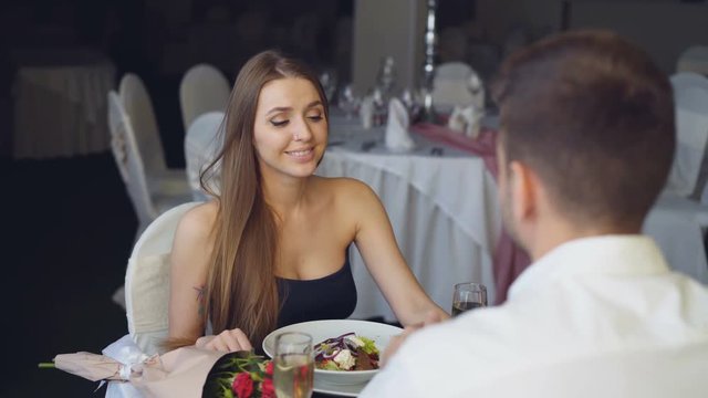 Handsome young man is proposing to surprised girl, then putting engagement ring on her finger, toasting and clinking glasses during romantic date in restaurant.