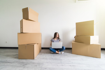 Young woman sitting on hardwood floor in new aprtmanet, using laptop next to cardboard box