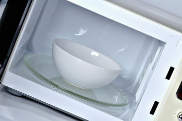 Inside of the microwave oven with clean empty white bowl