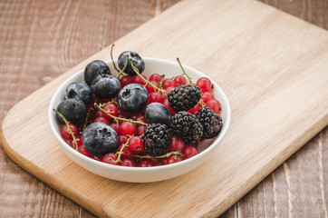 abundance berries in a white bowl/ abundance of berries in a white bowl on a wooden surface.