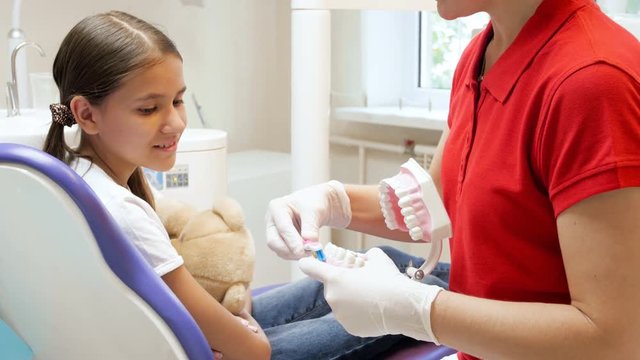 4k footage pf dentis tholding plastic model of teeth and talking to teenage patient