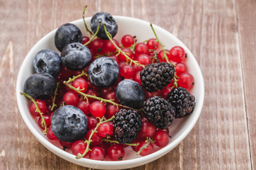 berries in a white bowl/ abundance of berries in a white bowl on a wooden background. Top view