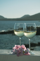 Two glasses with cold white wine served outside on terrace with pink tropical flowers, luxury resort with sea view, romantic vacation