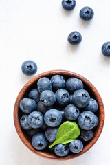 Organic blueberries in bowl with green leaf on white background. Top view. Flat lay, food pattern. Concept of vegan, healthy lifestyle, freshness, summer, harvest, natural foods.