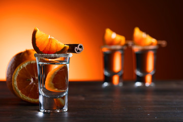Glasses of tequila with orange and cinnamon sticks on a wooden table.