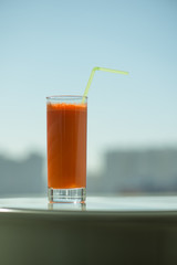 A glass of carrot juice with a straw in the cafe through the window on the background city